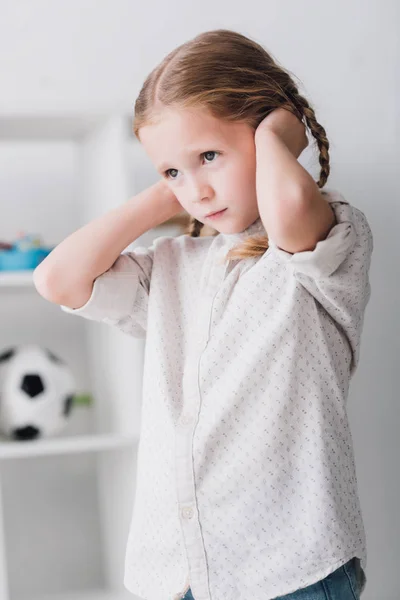 Close-up portrait of depressed little kid covering ears with hands and looking away — Stock Photo