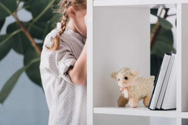 Scared little child standing behind bookshelves and crying — Stock Photo