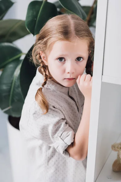 Effrayé petit enfant debout derrière les étagères et regardant la caméra — Photo de stock