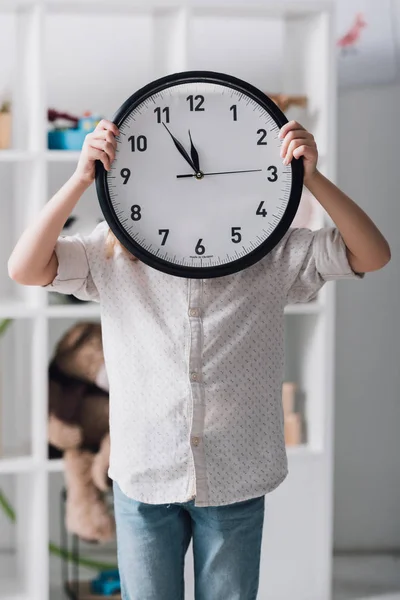 Niño pequeño cubriendo la cara con un reloj grande - foto de stock