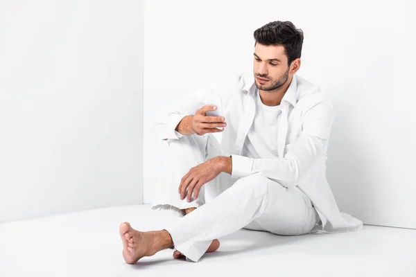 Erwachsener schöner Mann sitzt auf dem Fußboden und benutzt Smartphone — Stockfoto