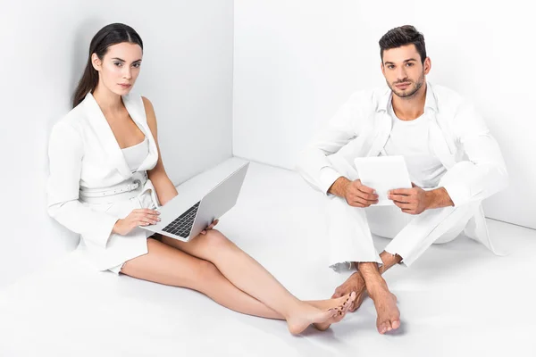 Adult couple in total white sitting on floor and using digital devices — Stock Photo