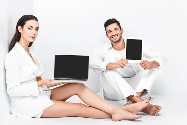 Adult couple sitting in white room with laptop and digital tablet — Stock Photo