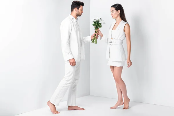 Bel homme en blanc total donnant des fleurs à une femme douce — Photo de stock