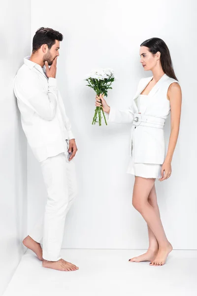 Schöne Frau in ganz Weiß, die dem überraschten Mann einen Blumenstrauß schenkt — Stockfoto