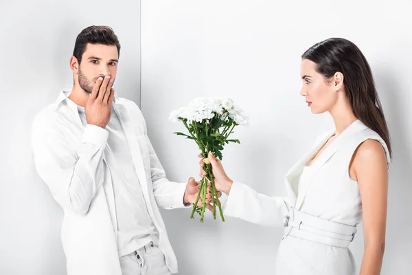 Close up of beautiful woman in total white giving bouquet of flowers to surprised man — Stock Photo