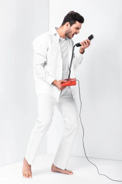 Angry barefoot man in total white screaming in retro telephone handset — Stock Photo