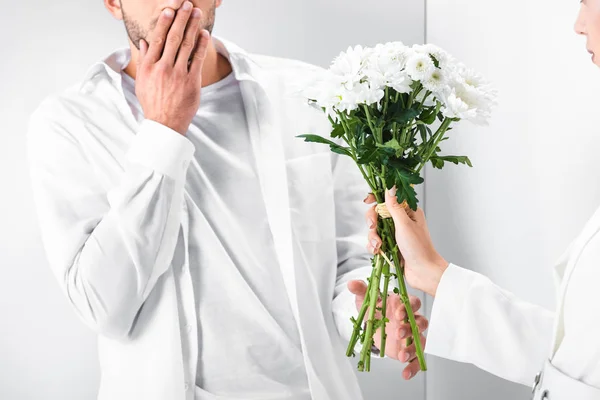 Close up of woman in total white giving bouquet of flowers to surprised man — Stock Photo