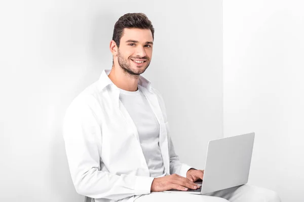 Adulto sonriente guapo hombre en total blanco usando laptop - foto de stock