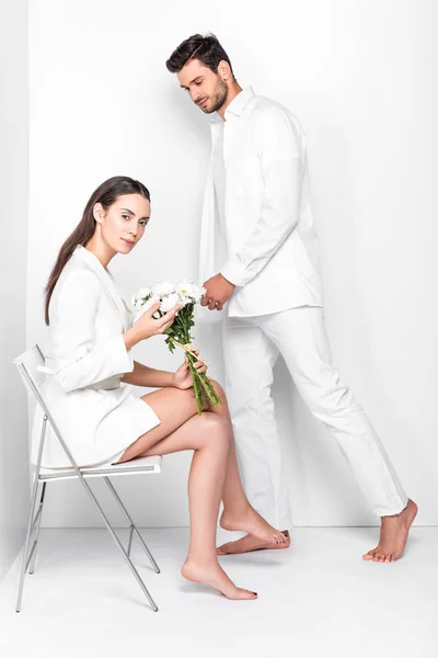 Adulte femme assis sur chaise avec bouquet tandis que l'homme posant en blanc total — Photo de stock
