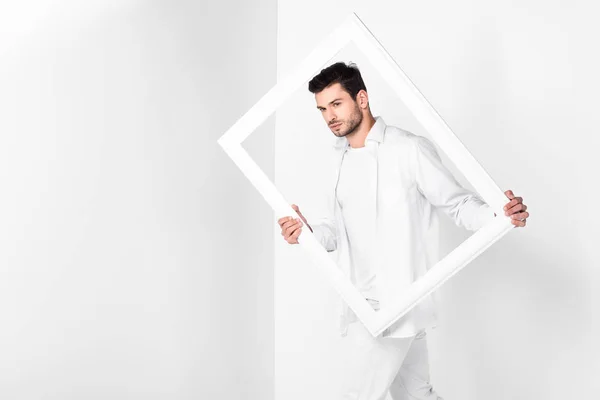 Handsome adult man in total white holding frame — Stock Photo