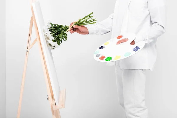 Primo piano di artista maschile in total white disegno su cavalletto con fiori — Foto stock