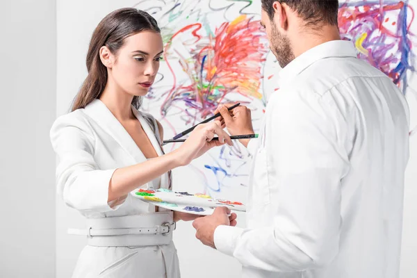 Close up of adult couple in total white drawing together with paintbrushes on clothes — Stock Photo