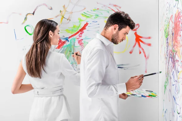 Close up of couple in total white drawing with paints on wall — Stock Photo