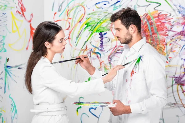 Colpo di studio di coppia in disegno bianco totale su vestiti con pennelli — Foto stock