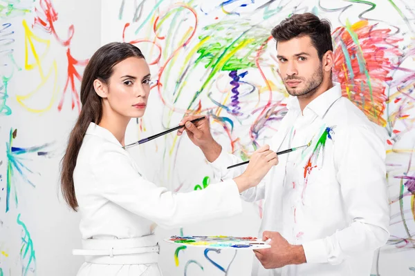 Studio shot of couple in total white drawing on clothes with painbrushes — Stock Photo
