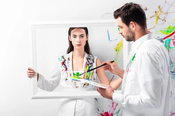 Mujer adulta de pie con marco blanco mientras el hombre sostiene el equipo de dibujo - foto de stock