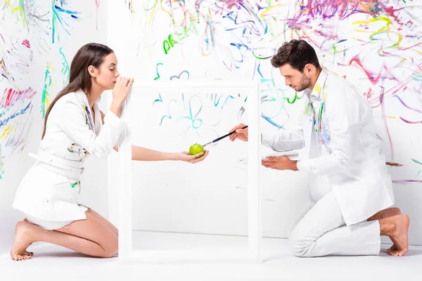 Barefoot couple painting apple in frame with paintbrush — Stock Photo