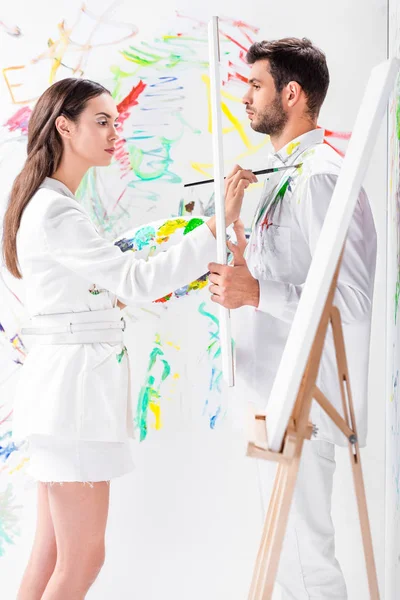 Hombre adulto sosteniendo marco blanco mientras que la mujer pintando ropa - foto de stock