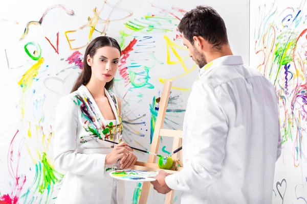 Adult couple in total white painting green apple on easel — Stock Photo