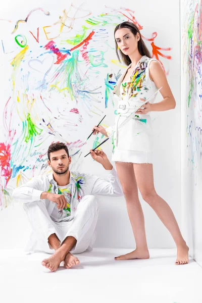 Barefoot couple in painted white clothes with drawing equipment — Stock Photo