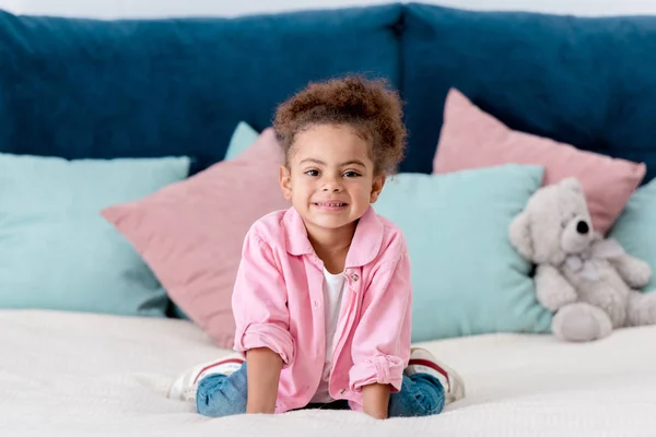 Lächelnd afrikanisches amerikanisches Kind auf dem Bett sitzend — Stockfoto