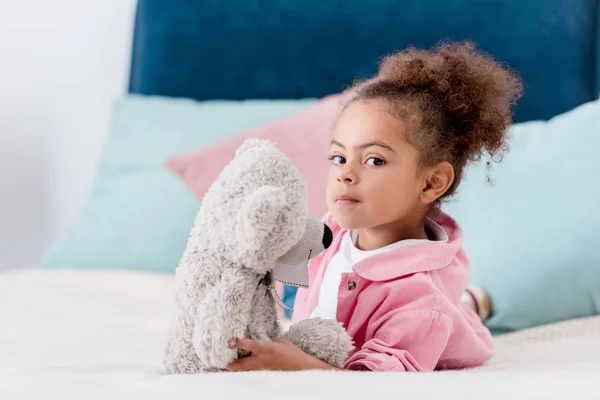 Süße afrikanisch-amerikanische Kind liegt auf dem Bett mit ihrem Teddybär — Stockfoto