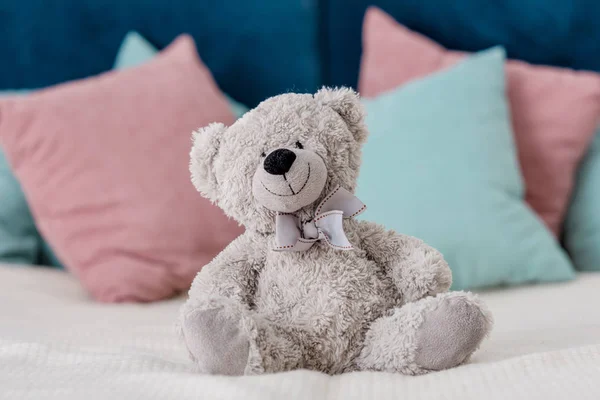 Vista horizontal cercana del oso de peluche sentado en la cama con almohadas en el fondo - foto de stock