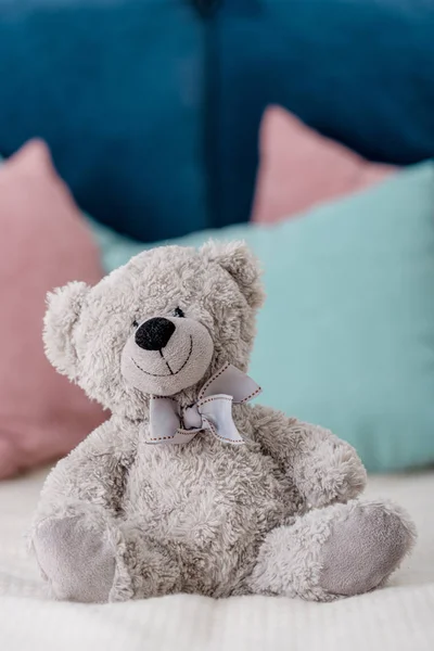 Close up vertical view of teddy bear sitting on the bed with pillows on background — Stock Photo