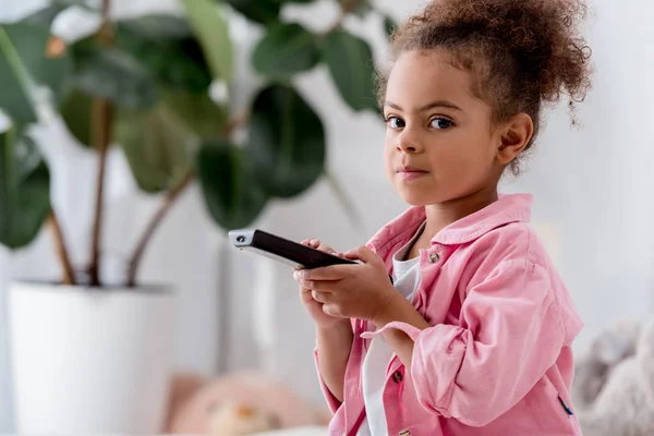 Primer plano de niño afroamericano sentado con control remoto de televisión - foto de stock