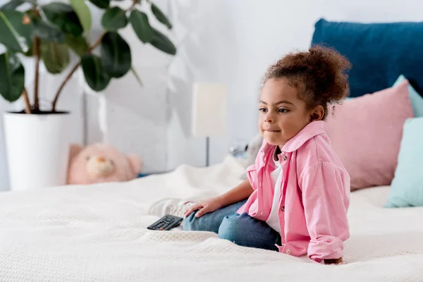 Entzückende afrikanisch-amerikanische Kind sitzt auf dem Bett und fernsehen — Stockfoto