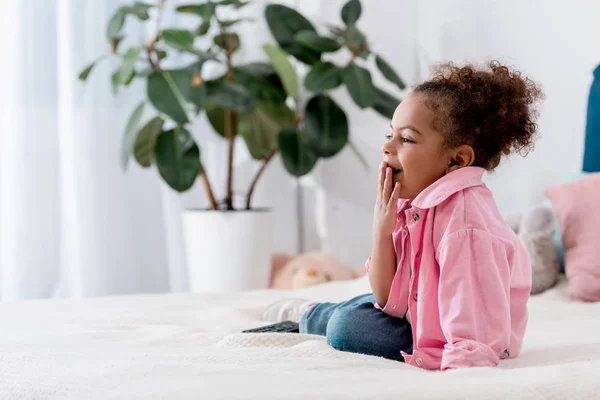 Süßes gähnendes afrikanisches amerikanisches Kind sitzt auf dem Bett — Stockfoto