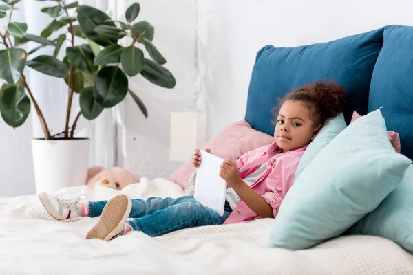 Entzückendes afrikanisch-amerikanisches Kind liegt mit digitalem Tablet auf dem Bett — Stockfoto