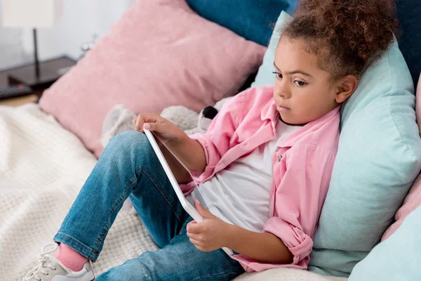 Thoughtful african american kid lying on the bed with digital tablet — Stock Photo