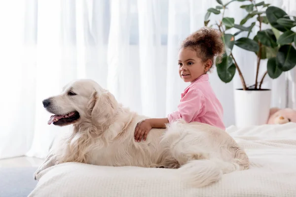 Adorable african american kid hugs her dog on the bed — Stock Photo