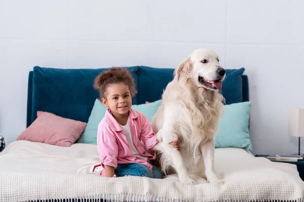 Cute african american kid sitting on the bed and holds dog paw — Stock Photo