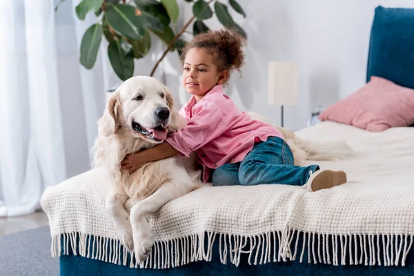 Mignon afro-américain gosse assis sur l 'lit et étreignant son chien — Photo de stock