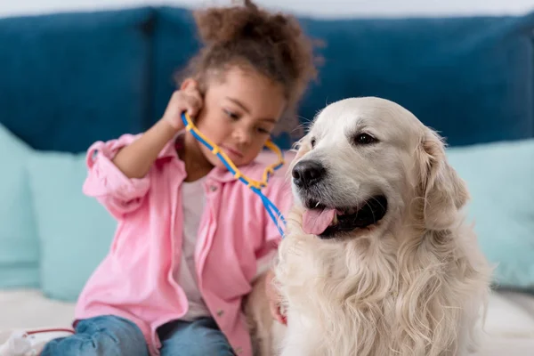 Adorable african american kid playing  with stethoscope and her retriever — Stock Photo