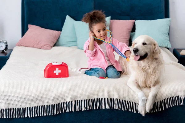 Lindo afroamericano niño jugando doctor con su golden retriever - foto de stock