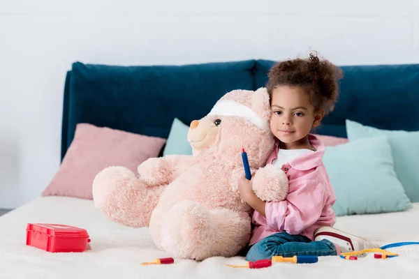 Pequena criança afro-americana de jaqueta rosa jogando o médico com ursinho de pelúcia — Fotografia de Stock