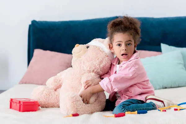 Little african american child in pink jacket playing the doctor  with teddy bear — Stock Photo