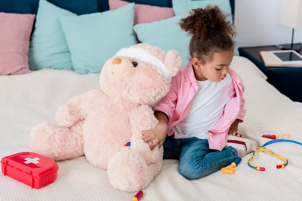 Маленький афроамериканець дитини в рожевий жакет грає лікар з ведмедиком — стокове фото