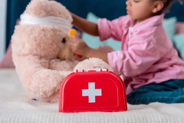 Little child in pink jacket examining teddy bear — Stock Photo