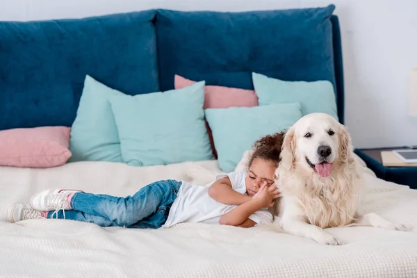 Miúdo afro-americano bonito deitado na cama e inclinado para o cão — Fotografia de Stock