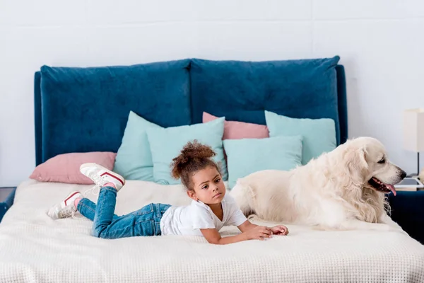 Bonito menino afro-americano pequeno com cão feliz deitado na cama — Fotografia de Stock