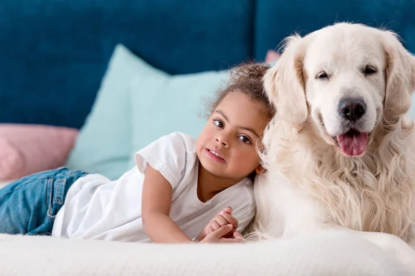 Adorable little african american kid with happy dog lying on bed — Stock Photo