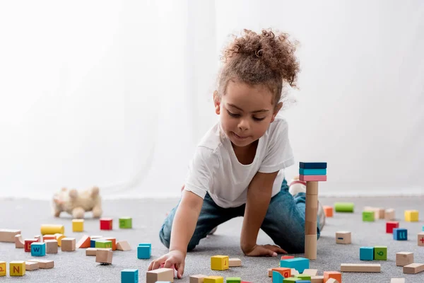 Criança americana africana adorável em camiseta branca brincando com cubos de brinquedo coloridos — Fotografia de Stock