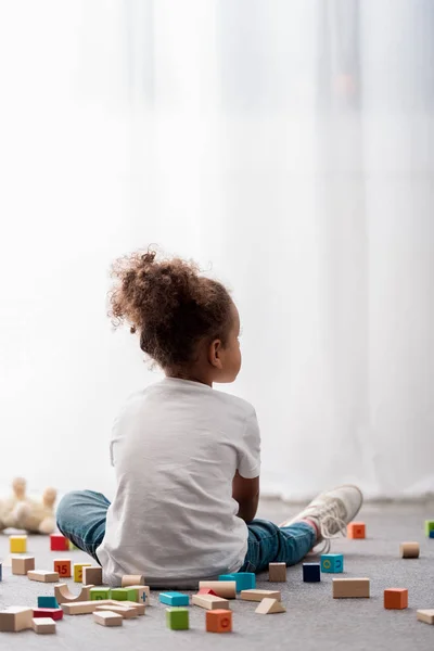 Vue arrière du petit enfant en t-shirts blancs entourés de cubes de jouets colorés — Photo de stock