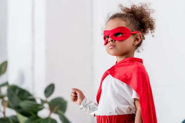 Ritratto di grazioso bambino afroamericano in costume da supereroe rosso e maschera — Foto stock