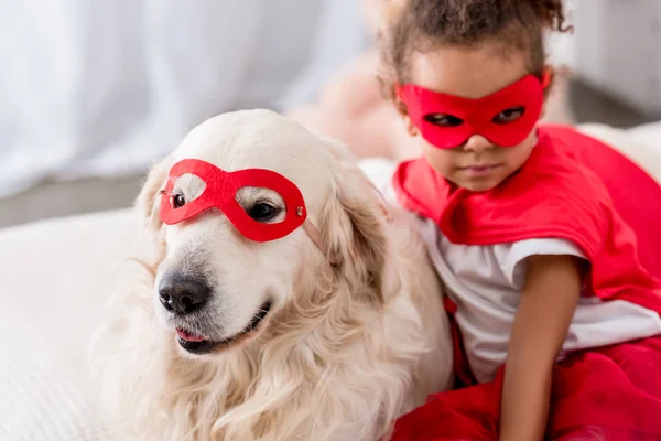 Adorable petit afro-américain avec chien en costumes de super-héros et masques rouges — Photo de stock